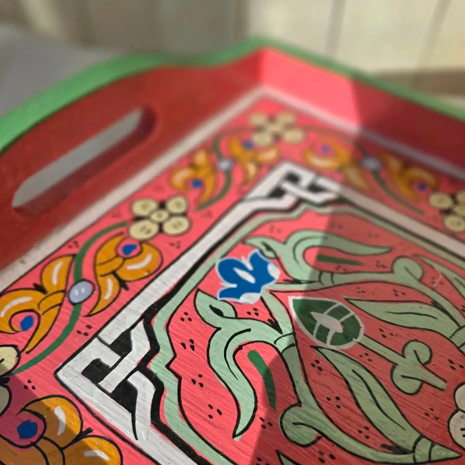 Plateau en bois de cèdre entièrement peint à la main dans un petit atelier à Marrakech.
Chaque pièce demande entre 8 et 9 heures de travail minutieux. Nous avons eu la chance de rencontrer un jeune artisan passionné qui a repris cet atelier. Il a la conviction que l’artisanat doit absolument se transmettre et être valorisé pour perdurer. Il s’engage pour que ces savoir-faire ne soient pas bradés, afin que les artisans puissent en vivre dignement.
Le bois choisi pour la confection de ce plateau est le bois de cèdre, sélectionné pour sa solidité et sa légèreté. L’artisan travaille ensuite au pinceau de calligraphie en poil d’âne, idéal pour un tracé précis et une application fluide de la peinture. Il dessine les motifs sans pochoir ni tracé préalable, avec beaucoup de patience, ajustant les couleurs à l’oeil.
Ce plateau en bois peint est aussi pratique que joli. Il est facile d’utilisation grâce à ses bords relevés et poignées. Idéal pour y servir thé et autres boissons, il peut aussi servir de décoration simplement posé sur une table ou un buffet avec quelques objets du quotidien. Ses couleurs et ses motifs en font en effet un bel élément à laisser visible, qui n’a pas besoin d’être rangé après usage.
Dimensions: Celui-ci mesure 34 x 24 cm