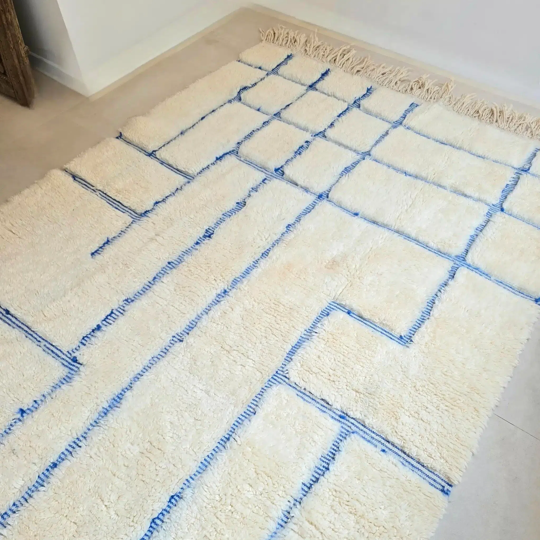 Tapis Berbère Beni Ouarain blanc cassé aux rayures bleues et motifs en relief, réalisé à la main dans les montagne du Haut Atlas Marocain, selon un savoir faire transmis de génération en génération. Il est en pure laine vierge de mouton.
Apportez du caractère et de la douceur à votre intérieur grâce à ce tapis Beni Ouarain fait main. Avec son blanc cassé et ses rayures bleues irrégulières, il s’intègre parfaitement à une décoration contemporaine ou plus classique. Tissé en laine épaisse, il allie authenticité et confort.
Sa texture dense et moelleuse est en effet idéale pour marcher pieds nus ou pour un espace cosy dans votre pièce à vivre.
Son design à la fois moderne et intemporel ainsi que la qualité supérieure de sa laine en font un pièce qui vous suivra de nombreuses années. Les lignes bleues apportent une touche de fraîcheur qui rappelle les maisons de vacances méditerranéennes. Elles sont obtenues grâce à des techniques traditionnelles de teinture artisanale, soulignant l’authenticité du tapis.
Placez-le dans un salon pour structurer l’espace et apporter une ambiance chaleureuse ou dans une chambre pour un effet cocooning. Dans une entrée, il devient un élément décoratif fort qui donne le ton dès l’arrivée.
Dimensions : Il mesure 265 x 160 cm environ
