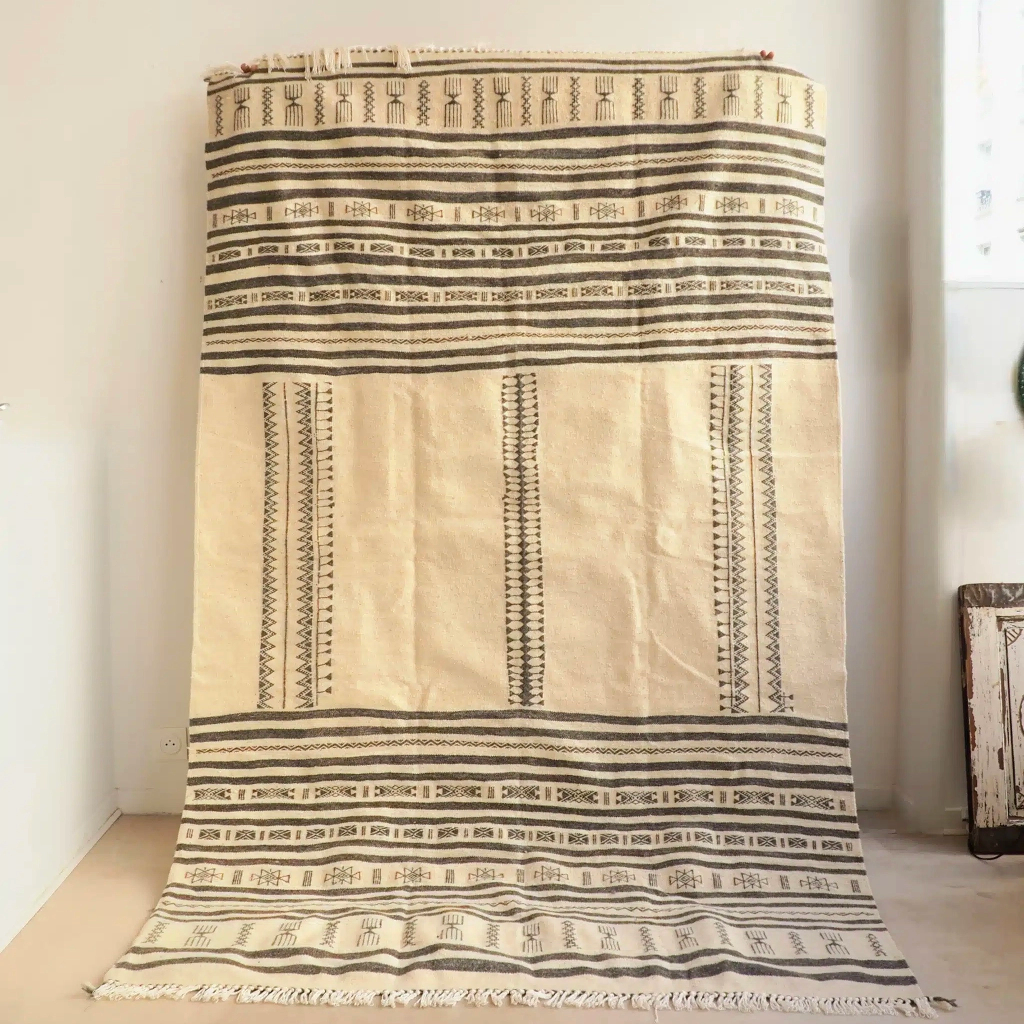 Tapis kilim Amazigh d’Algérie gris clair et blanc écru, tissé à la main à Beni Isguen, au cœur de la région de Ghardaïa, qui reflète l’héritage culturel de la vallée du M’zab. Réalisé en pure laine, il perpétue les savoir-faire ancestraux des artisanes mozabites, tra…
Les motifs uniques de ce tapis, appelés Ben Isguen, se distinguent par leur précision géométrique et leur harmonie. Ils incarnent l’esthétique minimaliste et raffinée propre à cette région. Ce tapis aux tons neutres s’adapte à tous type d’appartement/maison, dans un salon, une entrée, une chambre en descente de lit ou tête de lit.
Dimensions : 250 x 160 cm environ