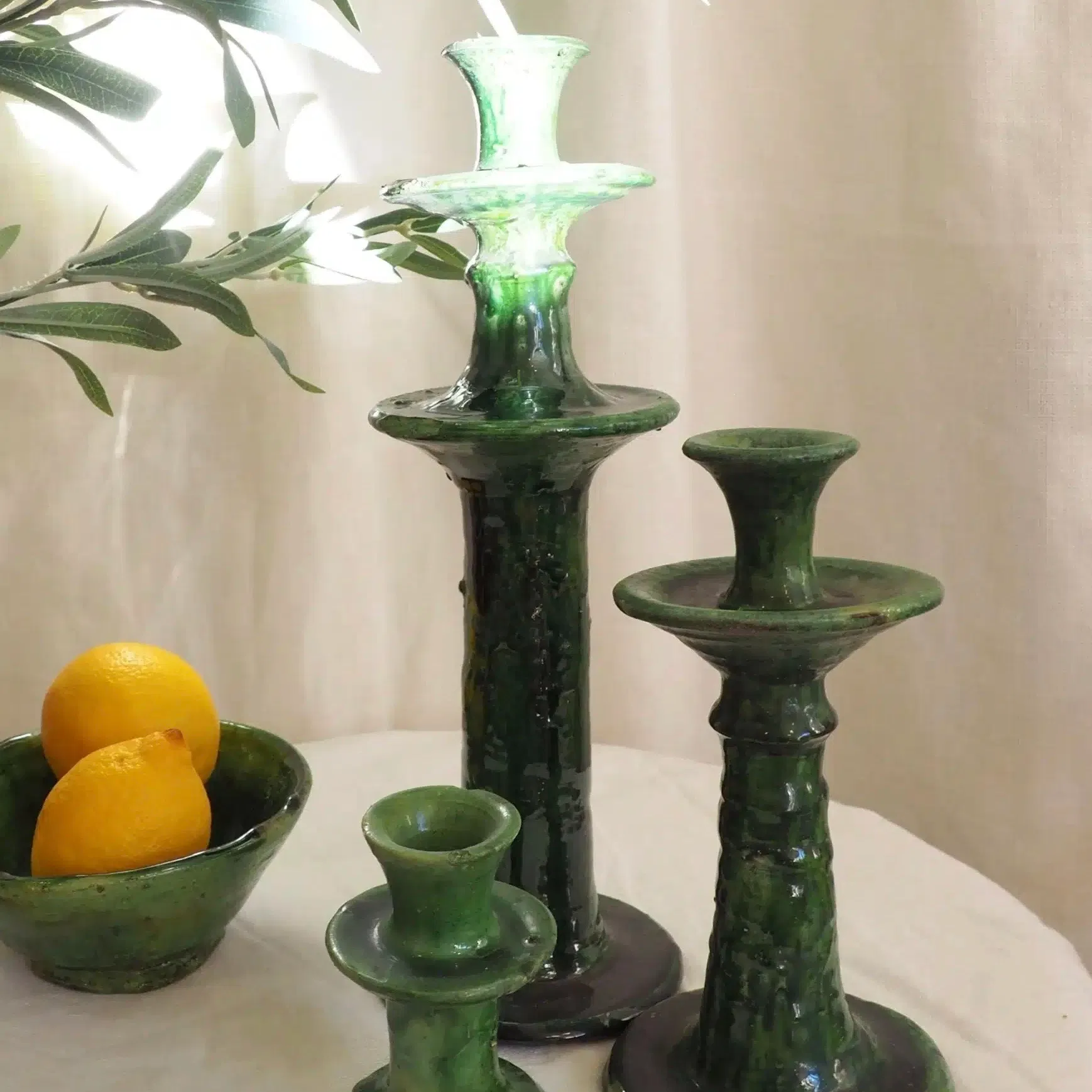 Bougeoir traditionnel Marocain Tamegroute vert émaillé réalisé à la main.
Ajoutez une touche authentique et bohème chic à votre décoration d’intérieur grâce à ces objets uniques aux matières naturelles!
Ces poteries portent le nom du village où elles sont réalisées: Tamegroute. Seulement quelques familles les fabriquent aujourd’hui, selon un savoir-faire ancestral. Les artisans façonnent chaque pièce à la main et les enduisent ensuite d’un alliage de manganèse et de cuivre. C’est la cuisson à très haute température dans des fours anciens à bois, qui apporte leur couleur verte typique, qui varie ainsi d’intensité à chaque pièce.
Veuillez noter qu’aucune pièce n’est parfaite: fissures, coulures, bosses, asymétries, etc font partie intégrante des poteries de Tamegroute. La couleur verte diffère à chaque objet, de clair à foncé, et peut parfois ne pas recouvrir la pièce en totalité, laissant ainsi découvrir l’argile.
Ils trouveront leur place dans toutes les pièces de la maison. Disposez les seuls ou en accumulation, en jouant avec leurs différentes tailles, sur une table dans le salon, dans une chambre, sur un buffet, dans une salle de bain…