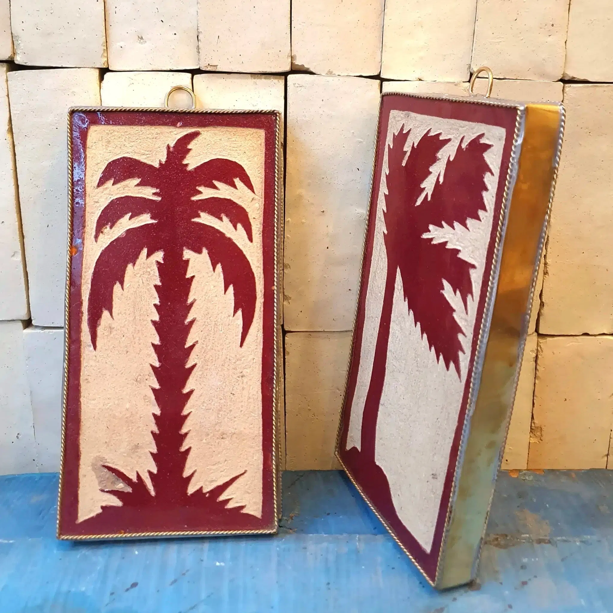 Décoration murale représentant un palmier bordeaux en pierre et céramique, cerclées de métal. Trois artisans différents doivent travailler sur ces objets pour leur création.
Les palmiers sont de formes et de couleurs différentes, choisissez celles que vous préférez, Palmier Medina ou Oasis!
Entièrement réalisés à la main dans un petit atelier au Maroc.
Accrochez-les grâce à leur attache prévue à cet effet, en utilisant un petit clou. Ou suspendez les à l’aide d’un fil en nylon transparent ou bien au contraire fluo pour ajouter du contraste et les personnaliser 😉
Vous pourrez les disposer seuls ou en accumulation, en jouant avec leurs coloris, à associer par exemple dans un pêle-mêle mural parmi des cadres, affiches, ex votos, etc… Ajoutez une touche de poésie à vos murs grâce à nos bijoux muraux!
Dimensions : Les décorations murales mesurent environ 20 x 10cm, et sont d’environ 1cm d’épaisseur. Les mesures peuvent varier d’un modèle à l’autre, chaque palmier étant fait main.
