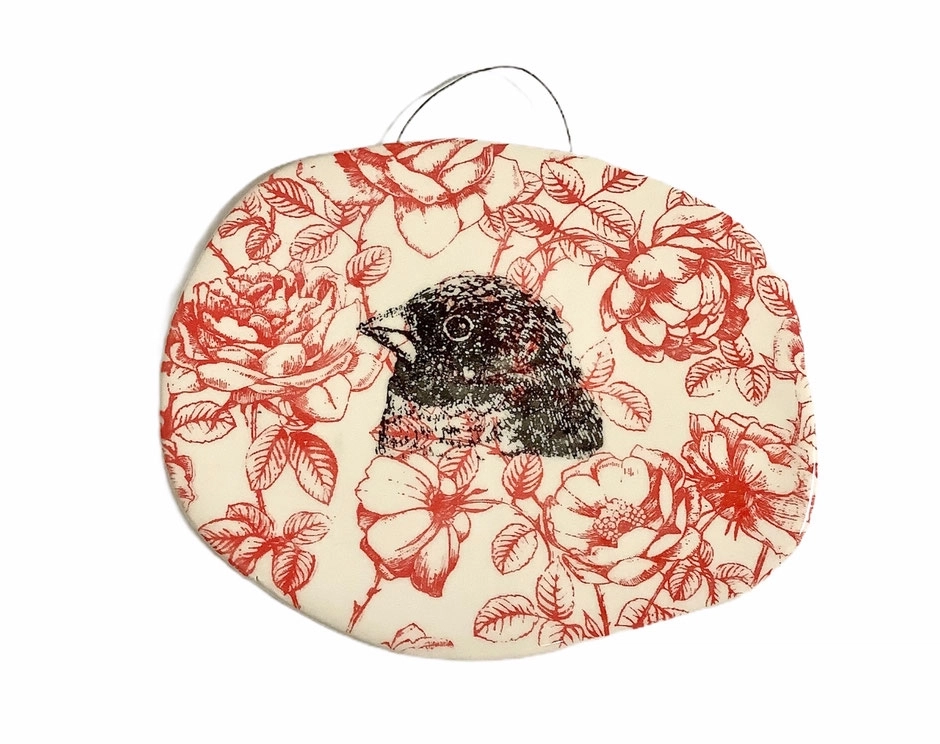 Cette plaque murale en céramique présente un délicat travail d'illustration : un oiseau noir finement dessiné, encadré d'un foisonnement de fleures rouges.