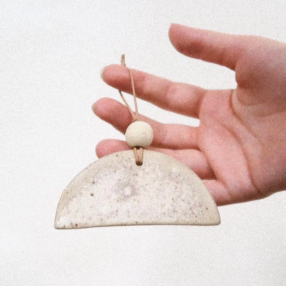 Diffuseur de douceur et de poésie, ce demi-cercle en céramique devient un compagnon discret du quotidien.
En grès beige ponctué de pyrites noires, au fini mat et brut sur une face, il se suspend dans une armoire, une entrée ou près d’un lit.
L’émail recouvre uniquement l’envers, laissant la face nue absorber délicatement les huiles essentielles que l’on y dépose.
Quelques gouttes suffisent pour créer une atmosphère apaisante, naturelle et subtilement parfumée.
Chaque pièce est unique, façonnée dans mon atelier à Paris avec attention.
DIMENSIONS : L 10cm, H 8 environ