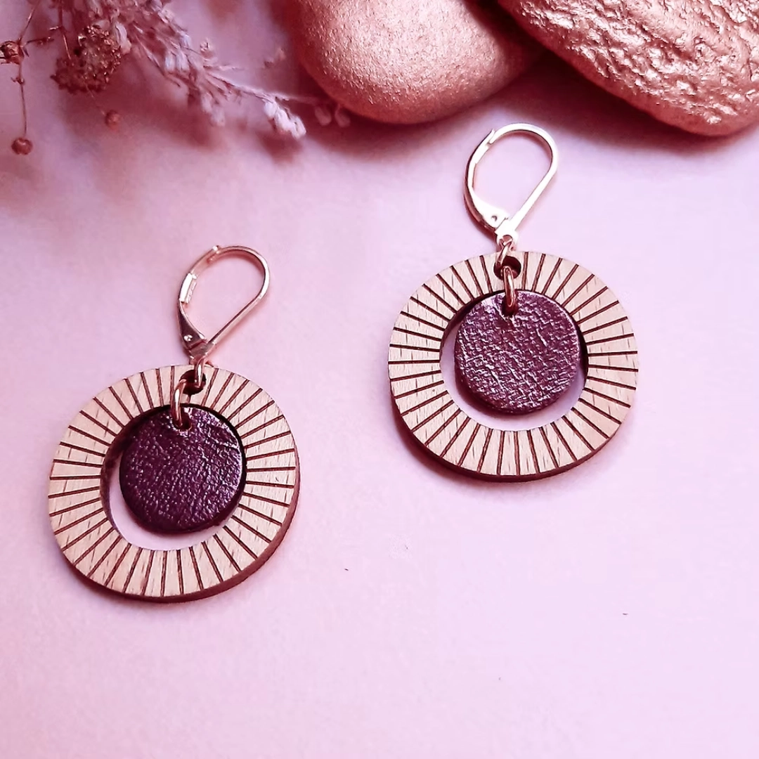 Boucles d'oreilles rondes, très légères à porter au quotidien. Les boucles pendantes BULLE Cassis se distinguent par leur volume arrondi et par leur style graphique travaillé, avec leurs petites rayures.
Laissez-vous charmer par ce bijou léger et aérien composé de bois éco-responsable et de cuir upcyclé. Boucles d'oreilles fantaisie, entièrement réalisées à la main dans notre atelier parisien. Boucles d'oreilles pour femme en bois naturel réhaussées d'un rond de cuir coloré dans une belle teinte violette mordorée. Fermeture par des dormeuses pour plus de sûreté.